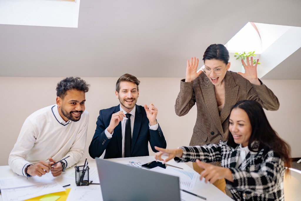 Excited team celebrating a success together at a laptop in the office